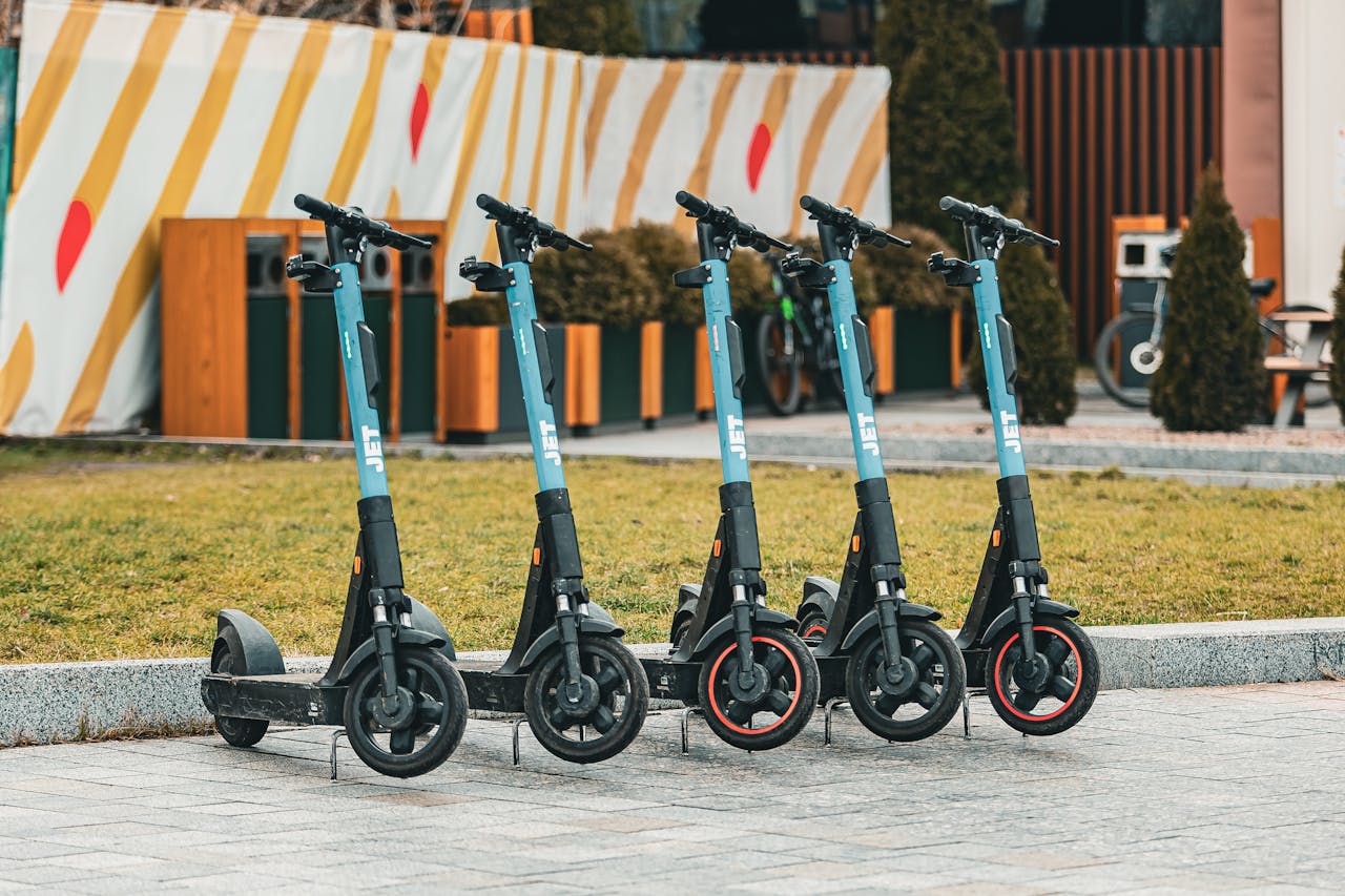 about-us-01 Group of five electric scooters neatly lined up outdoors, ready for rental use.