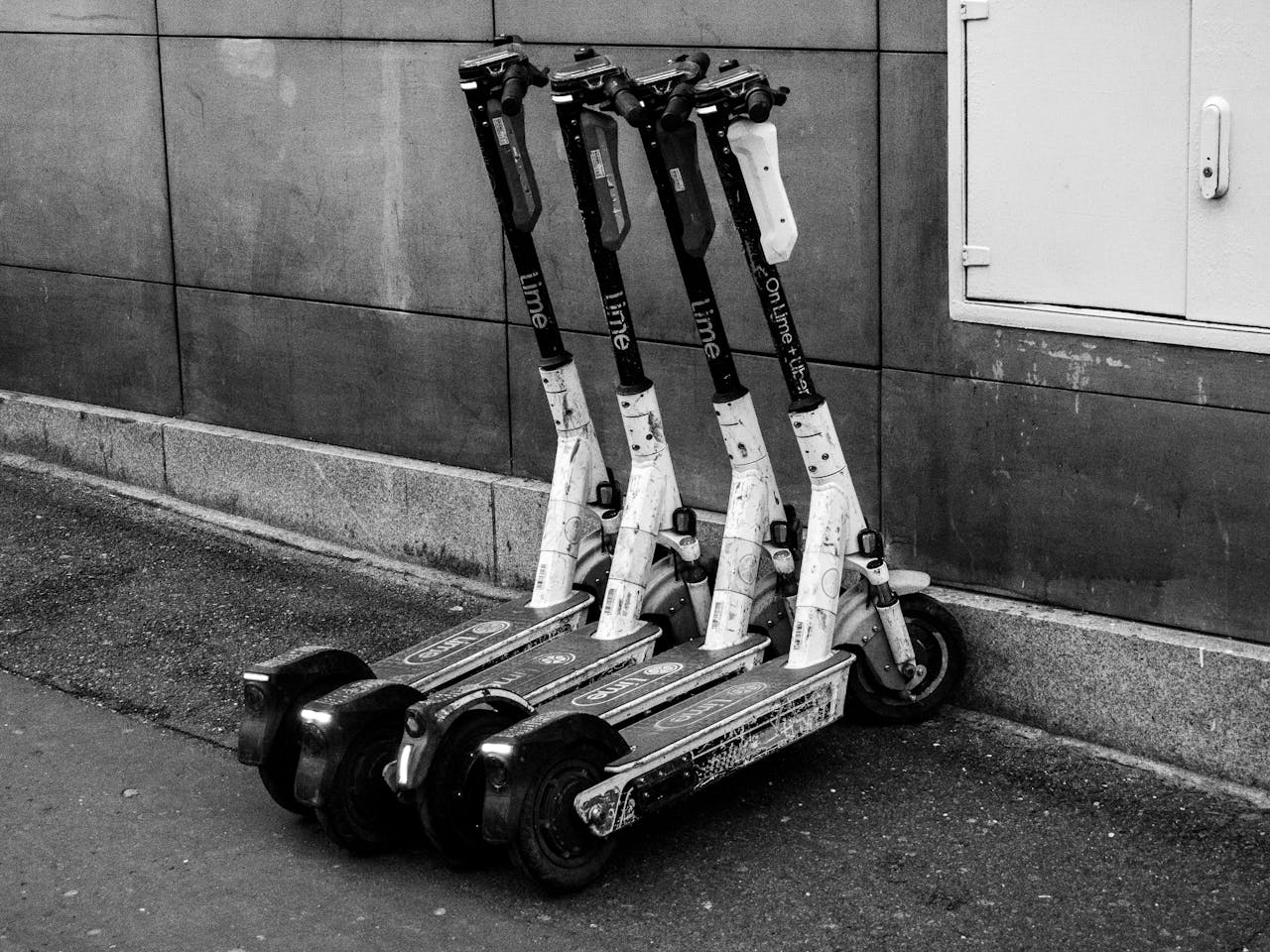 about-us-02 A group of electric scooters parked against a building wall, highlighting urban transportation.